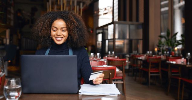 Smilende restaurantejer bruger bærbar computer og kreditkort i sin restaurant.