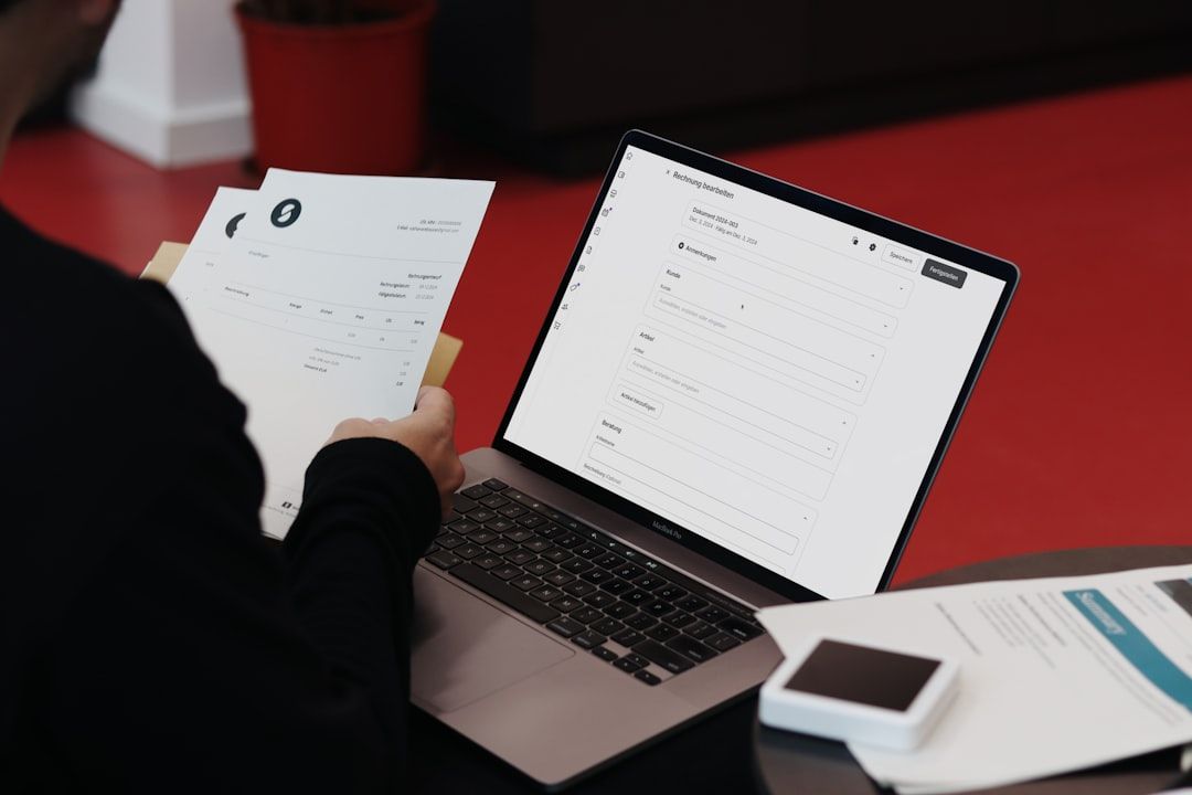 En person taster fakturaoplysninger ind på en bærbar computer fra et fysisk bilag.